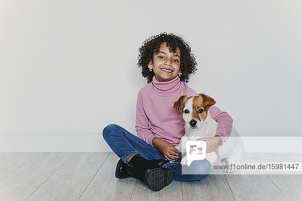 Portrait of smiling little girl sitting on the floor with her dog