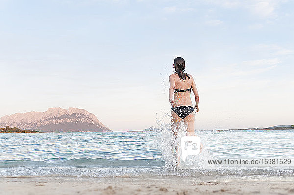 Rückenansicht einer Frau im Bikini  die ins Meer läuft  Sardinien  Italien