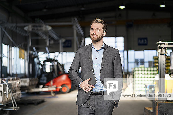 Young businessman with tablet walking in a factory