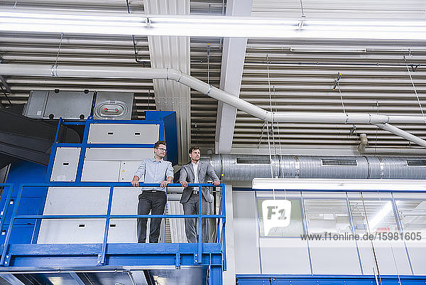 Two businessmen standing on upper floor in a factory