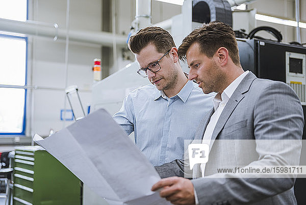 Two businessmen discussing a plan in a factory
