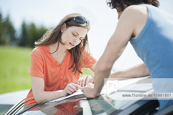 Selbstbewusste schöne Frau  die mit einem Mann auf dem Autodach eine Karte liest  während eines Sommerausflugs