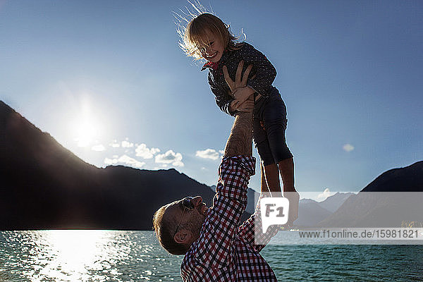 Vater hält seine fröhliche Tochter gegen den blauen Himmel am Achensee  Bundesland Tirol  Österreich  in die Höhe