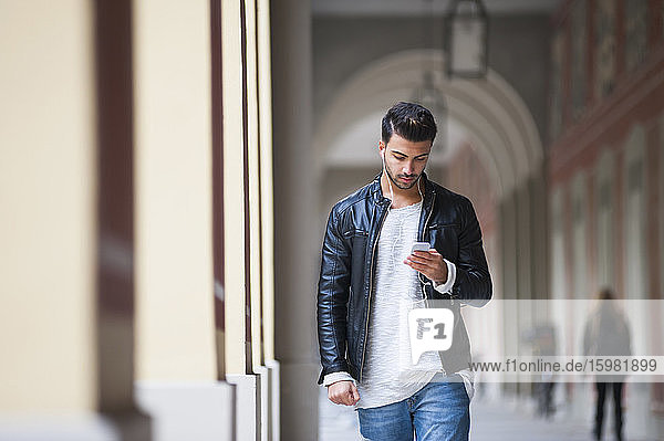 Junger Mann  der ein Smartphone benutzt  während er durch einen Korridor geht