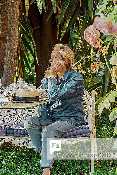 Portrait of senior woman sitting on garden bench looking at distance