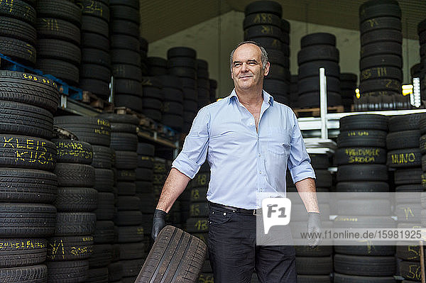 Confident senior male owner holding tire while working at store