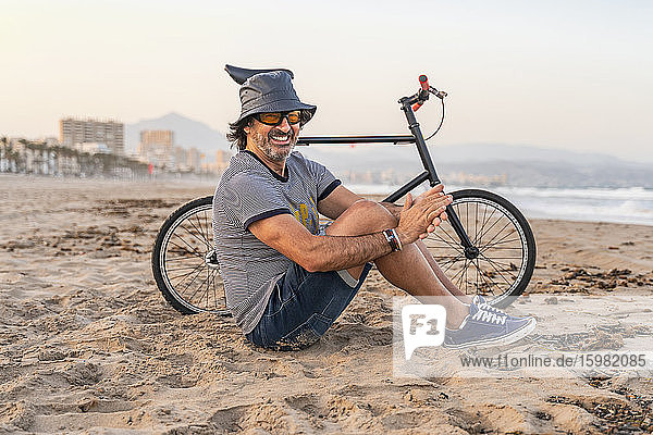 Mature man with bicycle  sitting on the beach  smiling