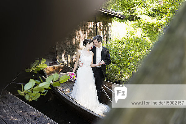 Romantisches frisch verheiratetes Paar im Boot stehend durch Holz gesehen