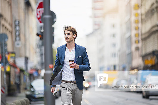 Portrait of young businessman with newspaper and coffee to go walking on the street