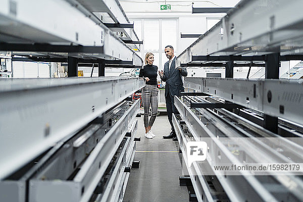 Geschäftsmann und Frau an Metallstäben in einer Fabrikhalle