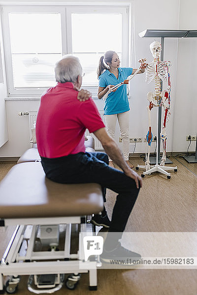 Physiotherapeutin erklärt dem Patienten die Behandlung anhand eines Skeletts