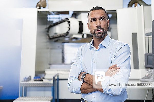 Porträt eines selbstbewussten Geschäftsmannes an einer Maschine in einer Fabrikhalle