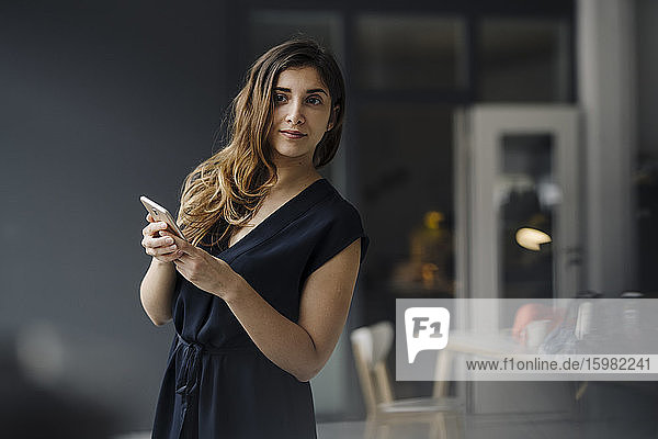 Porträt einer jungen Geschäftsfrau mit Smartphone  die etwas beobachtet