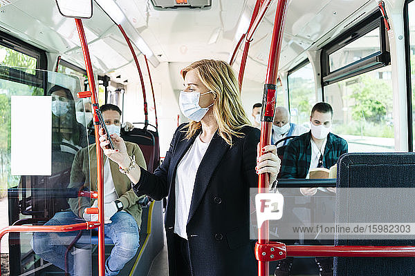 Geschäftsfrau mit Schutzmaske in einem öffentlichen Bus  die auf ihr Handy schaut  Spanien