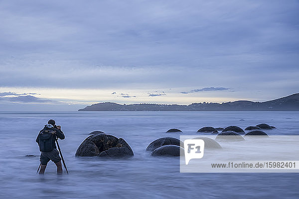 Neuseeland  Ozeanien  Südinsel  Südland  Hampden  Otago  Moeraki  Koekohe Beach  Moeraki Boulders Beach  Moeraki Boulders  Mann fotografiert runde Steine am Strand in der Abenddämmerung