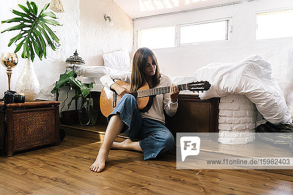 Frau sitzt auf dem Boden vor dem Bett und spielt Gitarre