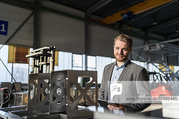 Porträt eines lächelnden jungen Geschäftsmannes mit Tablet in einer Fabrik