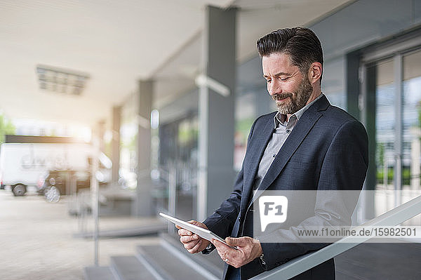 Smiling bearded entrepreneur looking at digital tablet while standing outside office building