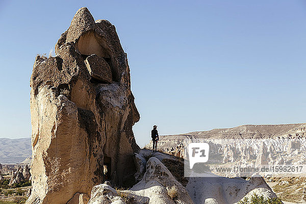Junge Frau steht auf einer Felsformation vor blauem Himmel in Goreme  Kappadokien  Türkei