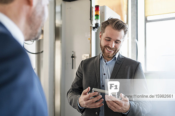 Smiling young businessman in a factory holding workpiece