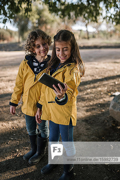 Lächelndes Mädchen nimmt Selfie mit Bruder von Smartphone im Freien