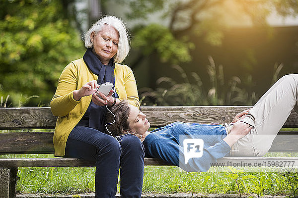 Ältere Frau und erwachsene Tochter entspannen zusammen auf einer Parkbank
