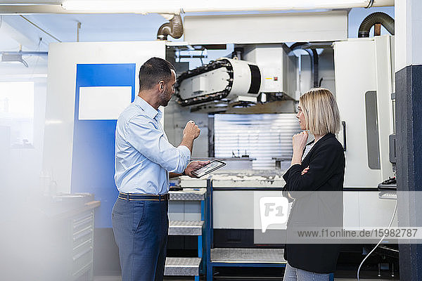 Geschäftsmann mit Tablet und Frau bei einer Besprechung an einer Maschine in einer Fabrikhalle