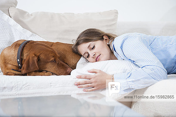 Schöne junge Frau schläft mit Hund auf Sofa im Wohnzimmer zu Hause