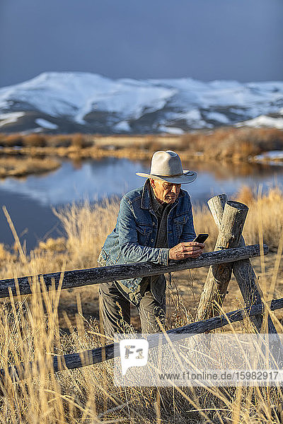 USA  Idaho  Sun Valley  älterer Mann mit Cowboyhut  der sich gegen den Zaun lehnt