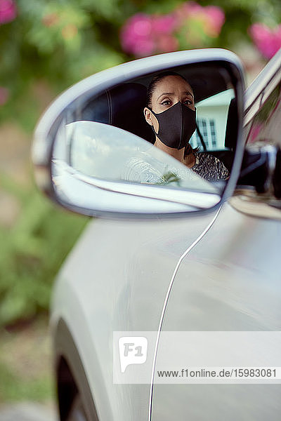 Frau mit Gesichtsmaske fährt Auto  das im Spiegel reflektiert wird