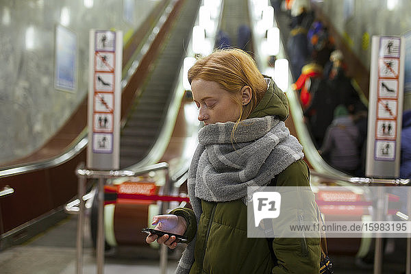 Russia  Novosibirsk  Young woman with smartphone standing by escalator