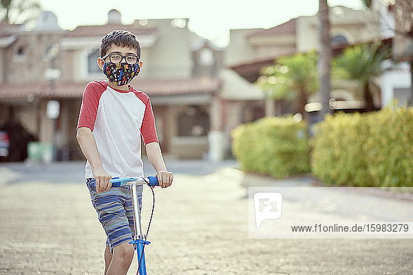 Mexiko  Zapopan  Junge mit Gesichtsmaske beim Rollerfahren