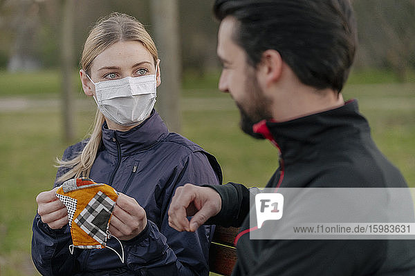 Junge Frau  die einem Mann während der Quarantäne im Park eine Gesichtsmaske gibt