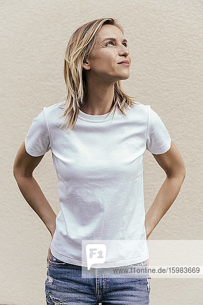 Porträt einer blonden Frau mit weißem T-Shirt  die vor einer hellen Wand steht und nach oben schaut