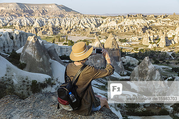 Rückansicht einer jungen Frau  die mit ihrem Smartphone die Landschaft in Goreme  Kappadokien  Türkei  fotografiert