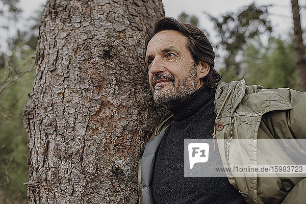 Mature hiker leaning on tree trunk