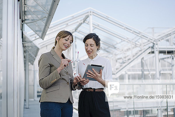 Two businesswomen with tablet and wind turbine model having a meeting at a greenhouse