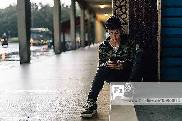 Young man using smart phone while sitting on steps against wall