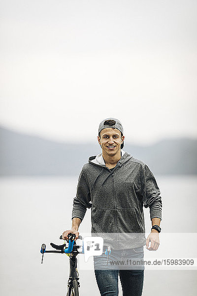 Lächelnder männlicher Sportler mit Rennrad gegen den klaren Himmel