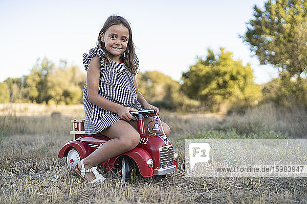 Portrait of smiling little girl with pedal car in nature