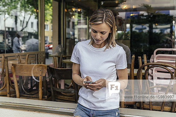 Porträt einer Frau  die vor einem geschlossenen Café eine SMS schreibt