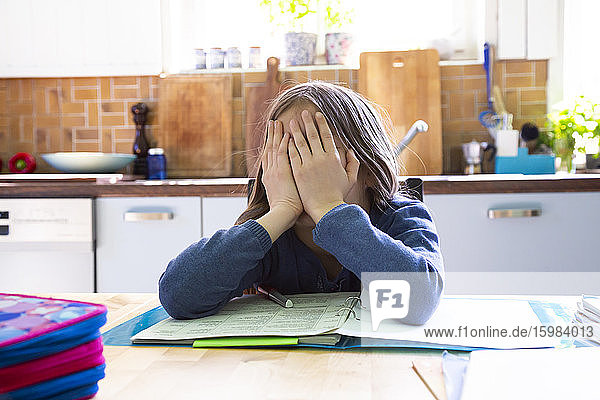 Girl doing homework in kitchen at home  hands on face