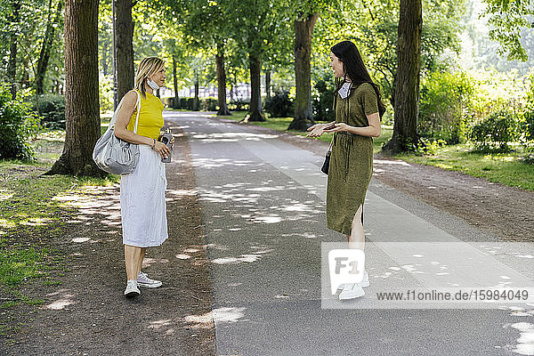 Two women meeting in nature with let down face masks