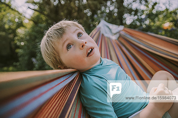 Cute boy looking up while relaxing on hammock at garden during sunny day