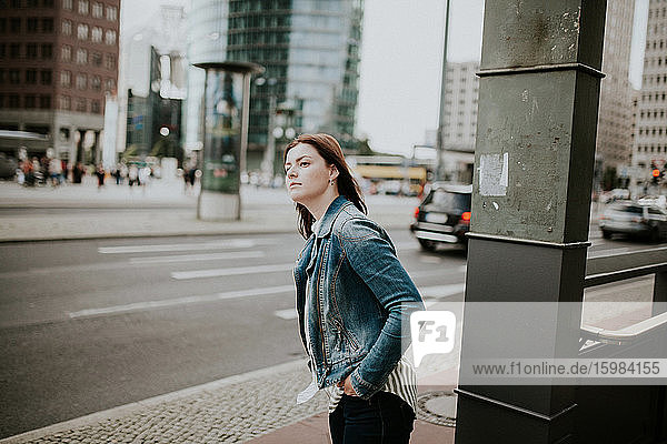Deutschland  Berlin  Porträt einer jungen Frau  die auf dem Bürgersteig wartet