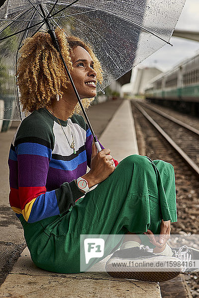 Junge Frau in voller Länge im Schneidersitz auf dem Bahnsteig während des Monsuns