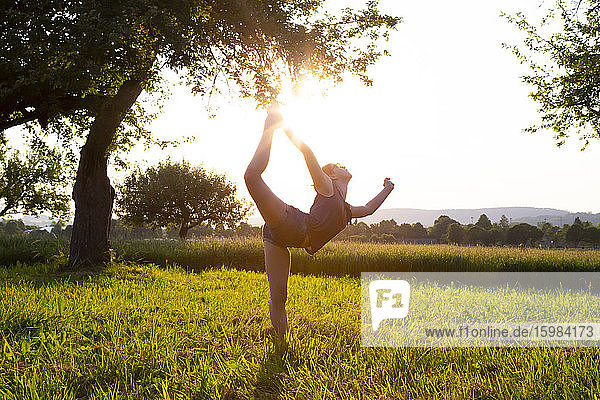 Teenage girl performing yoga in grassy field at sunset