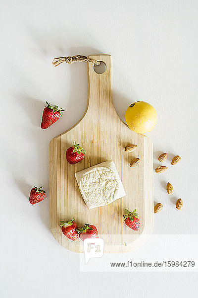 Wooden cutting board fresh strawberries almonds single lemon and homemade vegan cheesecake