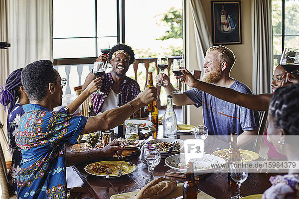 Smiling friends toasting drinks while sitting at dining table during lunch