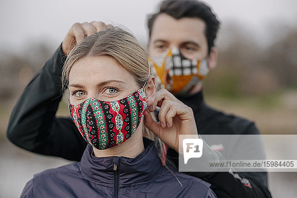 Porträt einer jungen Frau  während ein Mann im Park eine Gesichtsmaske für sie anpasst